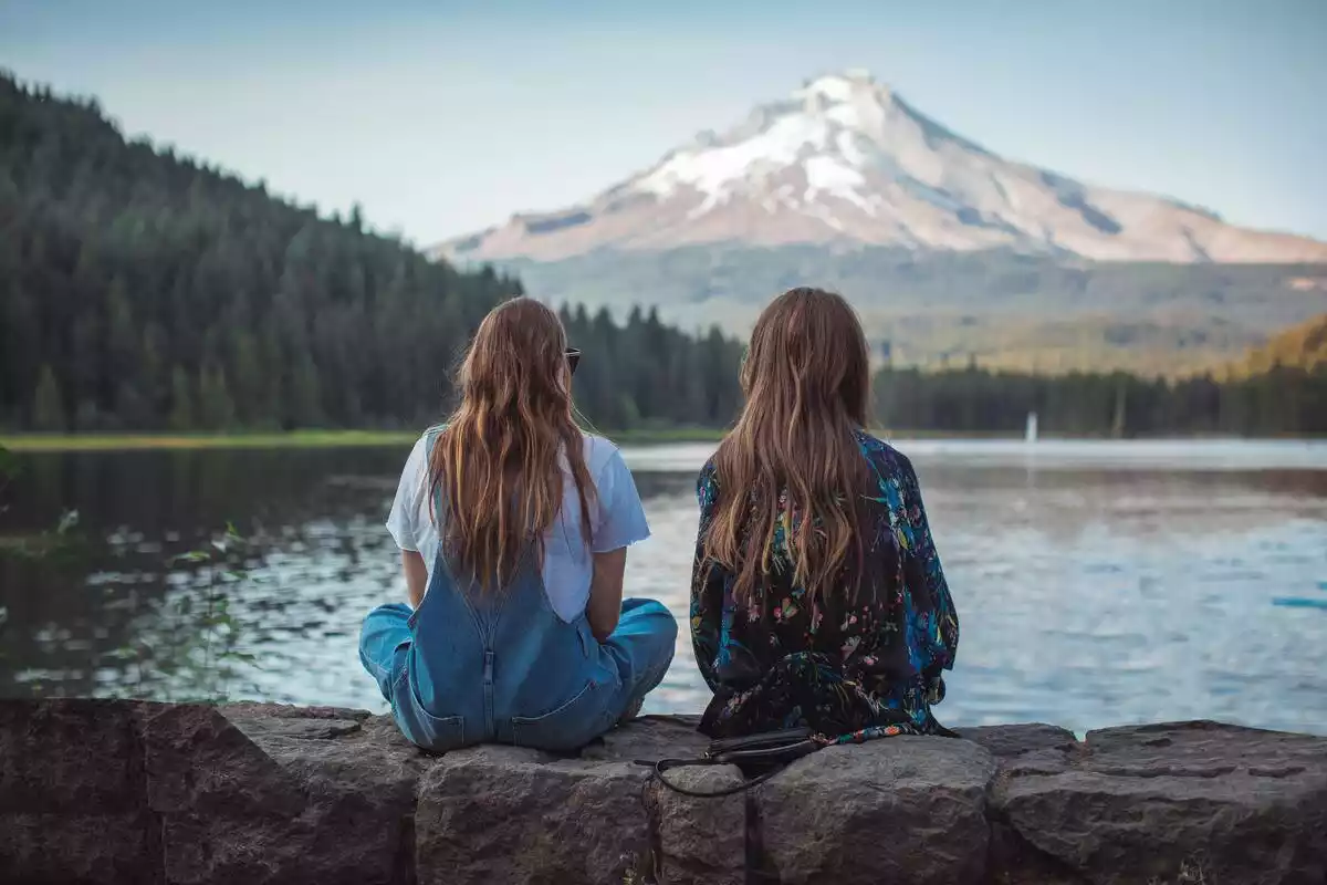 Dos chicas de espaldas frente a un lago y una montaña