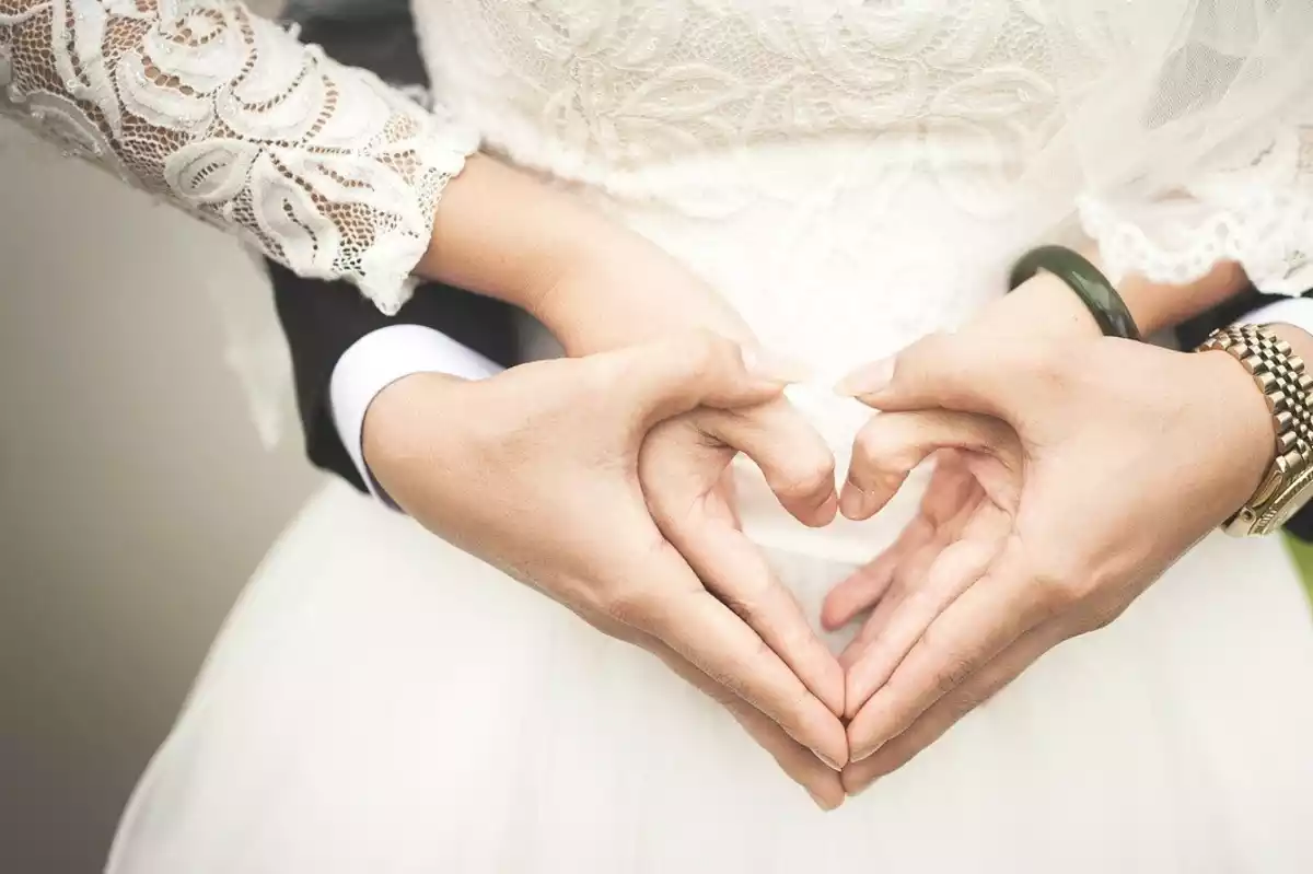 Una pareja de casados formando un corazón con las manos vestidos para la ocasión