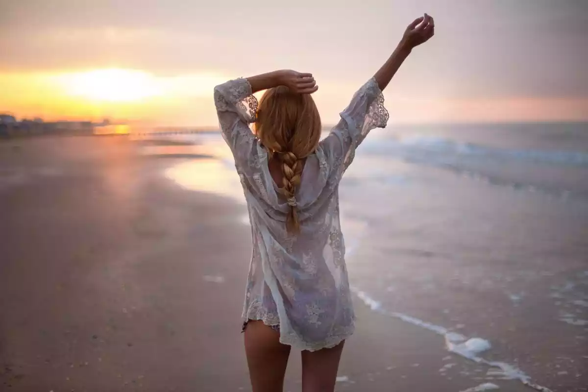 Una chica rubia de espaldas andando por la orilla del mar
